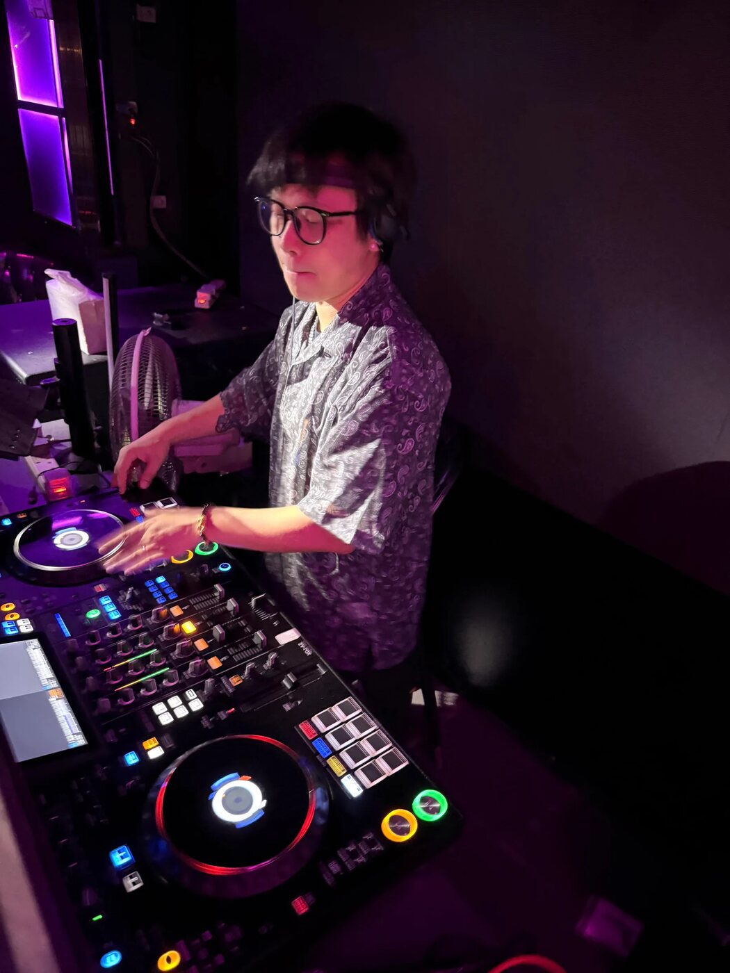 DJ 在活動現場的控制器前混歌,雙手放在播放轉盤與混音推桿上,旁邊是自帶的器材與電源線